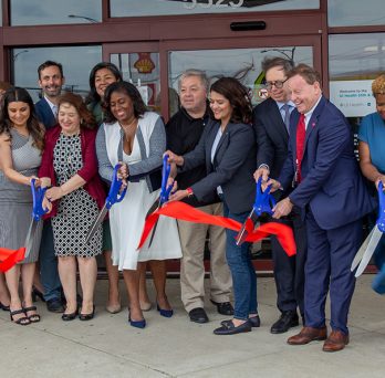 Health Collaborative leadership cutting a large red ribbon in front of the facility
                  