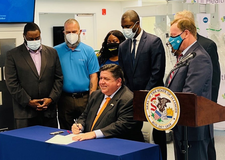 Dr. Robert Barish and other dignitaries watching as Governor Pritzker signs HB5318