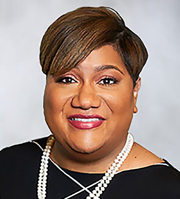 Rani Morrison wearing a black dress and pearls, and smiling into the camera