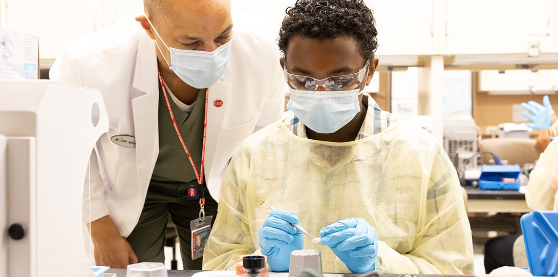 young Black main in mask and gown receiving guidance from a Black faculty member