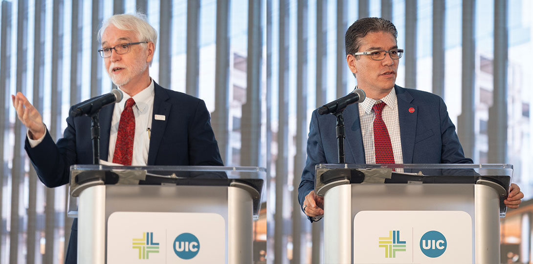 Timothy Killeen and Javier Reyes in formal suits, standing behind podiums with the UI Health logo on the front