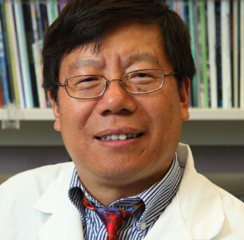 Dr. Lijun Rong in white lab coat posed in front of shelves of books 