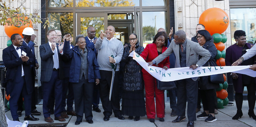 A group of happy people all participating in cutting a large ribbon in front of the building