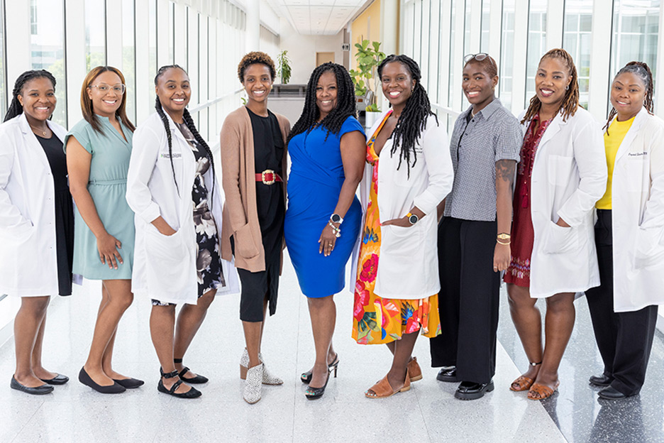 Nine African-American clinicians standing in a well-lit walkway in the hospital