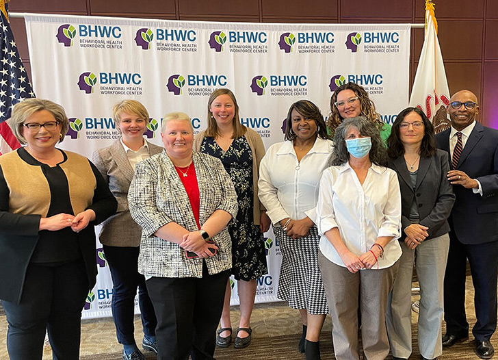 diverse group of people from the IBHE and UIC against a backdrop with the Behavioral Healthcare Workforce Center logo