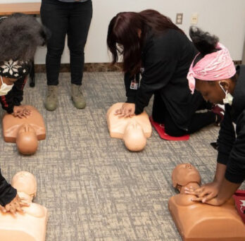 women of color engaging in CPR training on CPR mannequins with dark and light flesh tones 