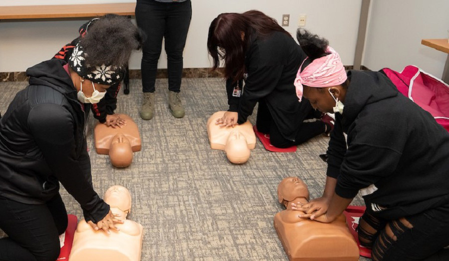women of color engaging in CPR training on CPR mannequins with dark and light flesh tones