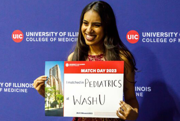 female student with brown hair holding a sign showing her residency match, in front of a backdrop with the College of Medicine logo