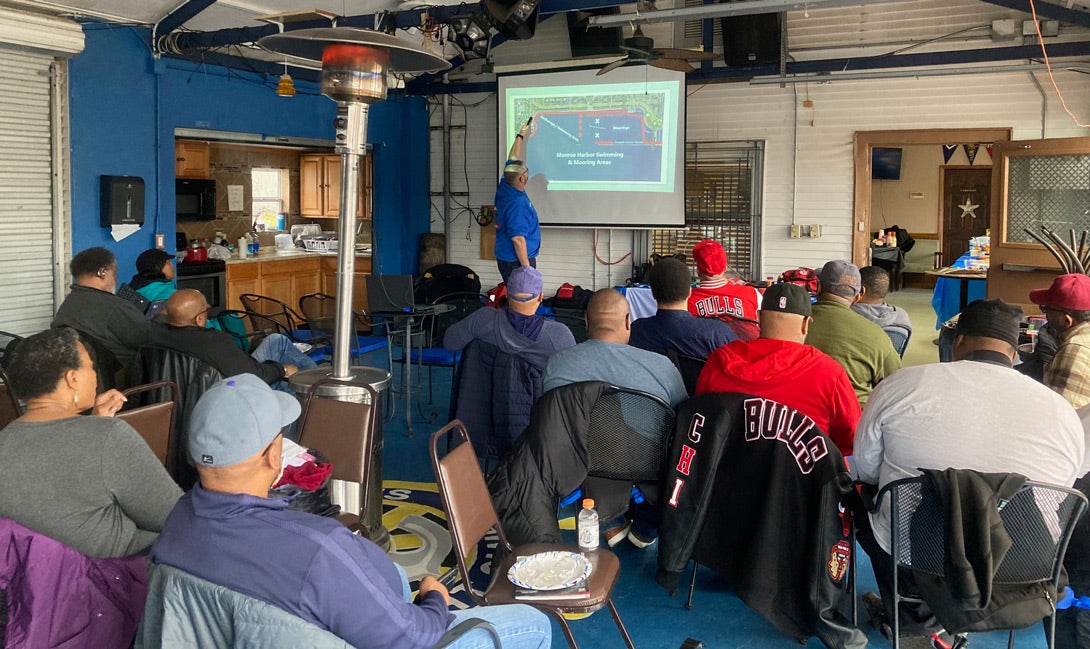 audience of people in a room, looking at man giving a presentation on boat safety training