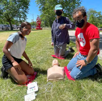 community members working with CPR training mannequin on a green lawn 