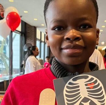 African American boy holding up a card with a drawing of a rib cage and a heart 