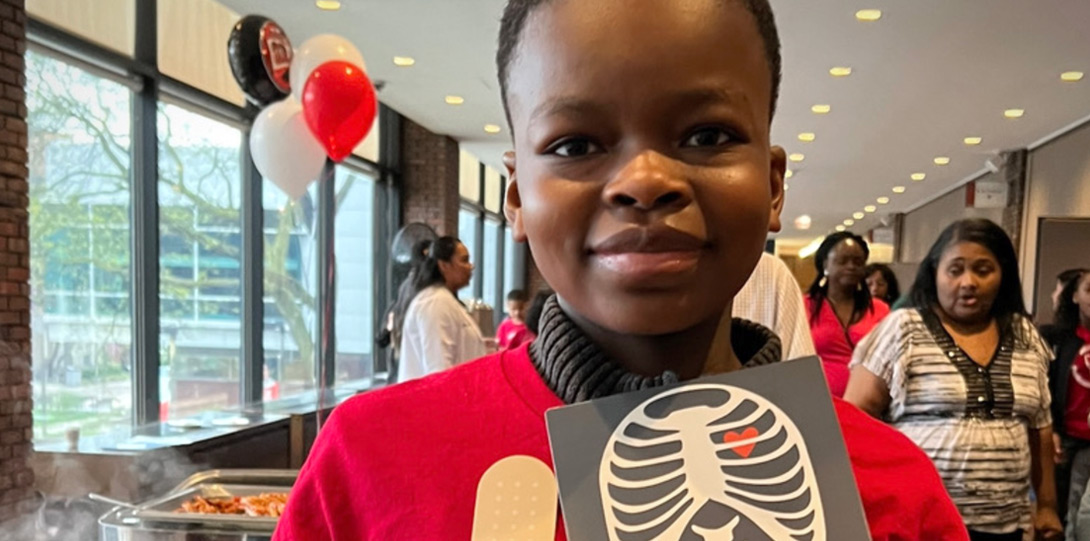 African American boy holding up a card with a drawing of a rib cage and a heart