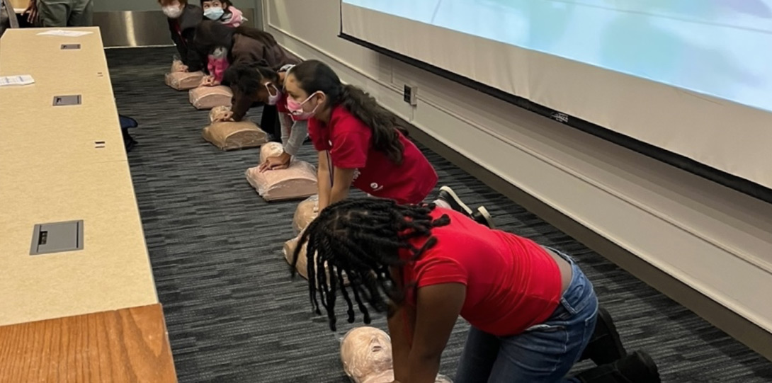 Middle schoolers kneeling over CPR mannequins, learning how to apply CPR