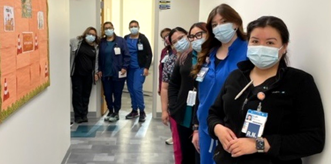 staff members wearing scrubs and masks, standing together in a clinic hallway