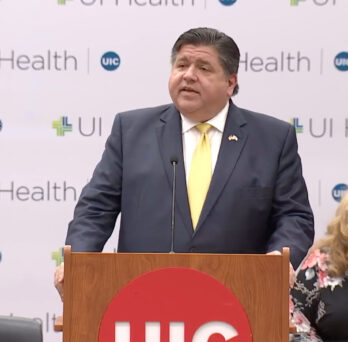 Illinois Governor Pritzker standing behind a podium with a large UIC logo on the front 