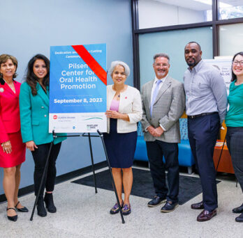 leadership and stakeholders in a bright modern space, next to a sign with a red ribbon and the name of the clinic 