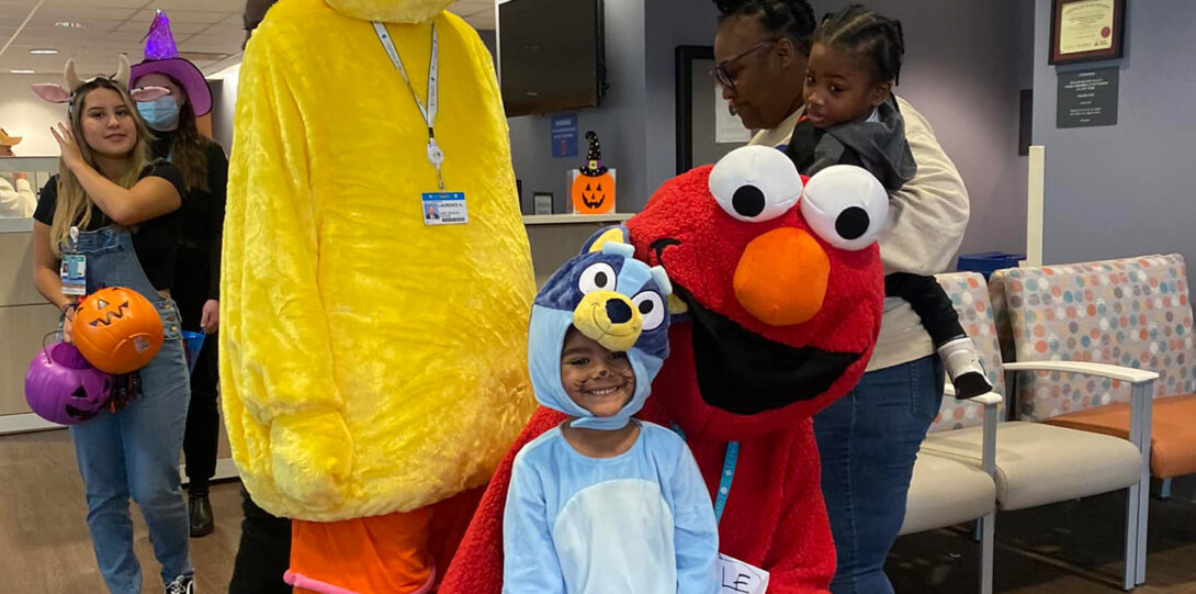 a young patient in a costume posing with Elmo and Big Bird