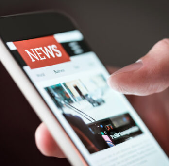 a person's hand holding a smartphone that is showing news 