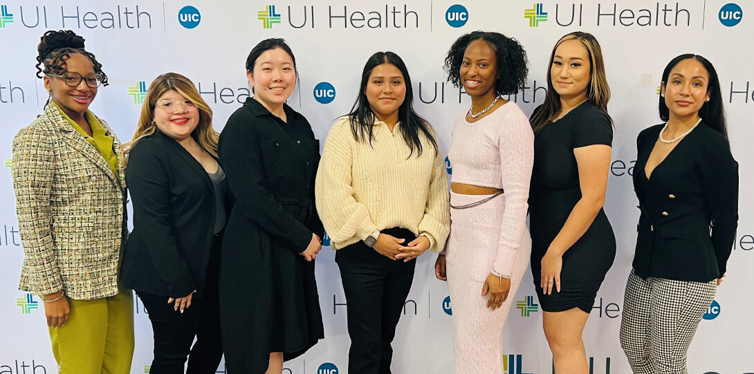 seven young women of color posing together in fron tof. aback drop of UI Health logos