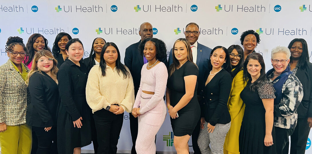 large diverse group of people posing together in front of a backdrop of UI health logos
