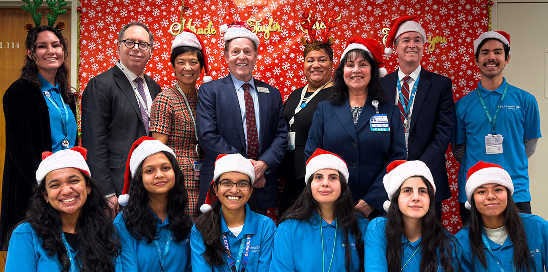 staff in b lie t-shirts and Santa hats posing with hospital leadership in front of a festive backdrop