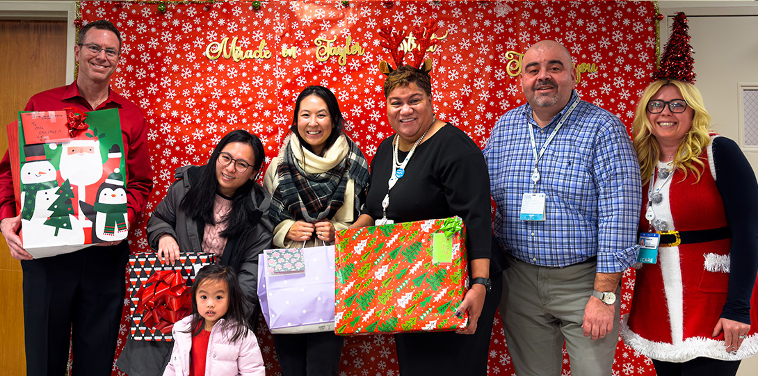 a diverse group of people in front of a festive backdrop and holding wrapped gifts