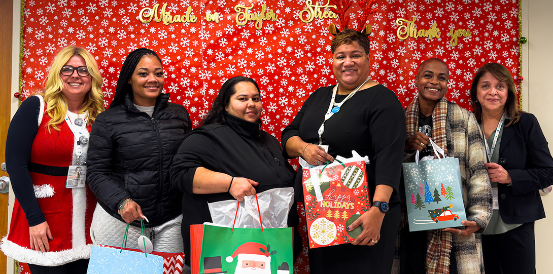 a diverse group of people in front of a festive backdrop and holding wrapped gifts
