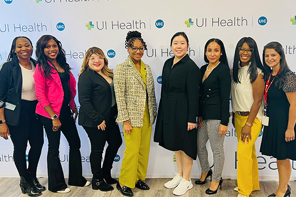 seven young women of color posing together in front of a background wiht UI health logos on it