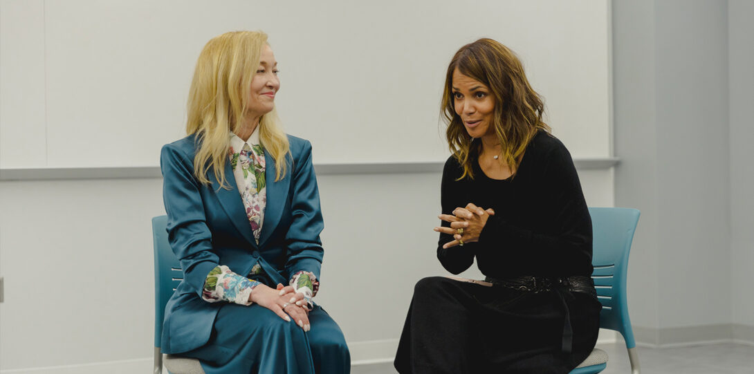 a blonde woman in a turquoise suit sitting next to Halle Berry as they converse