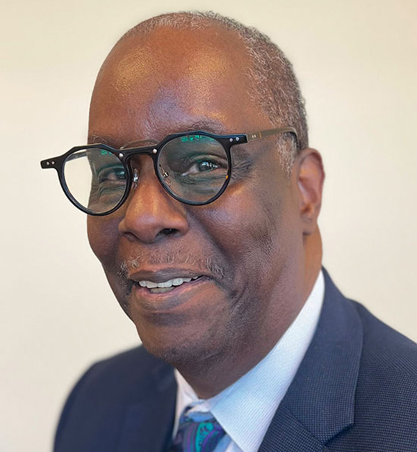 photo of African American man wearing glasses and a blue suit coat, white shirt and blue neck tie