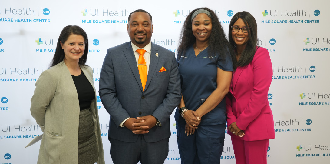 four people smiling and posing together in front of a backdrop of repeating UI Health logos
