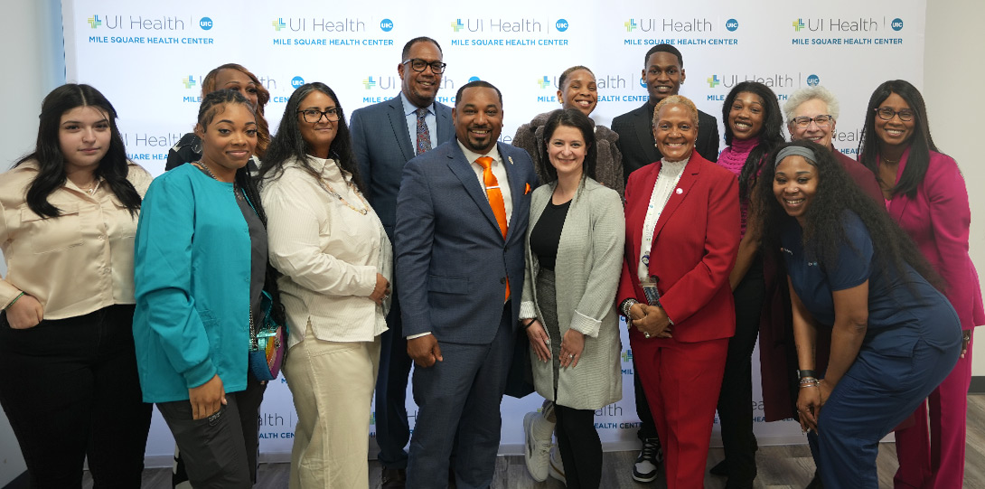 fourteen people smiling and posing together in front of a backdrop of repeating UI Health logos