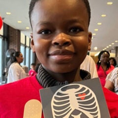 African American boy holding up a card with a drawing of a rib cage and a heart