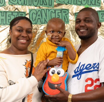 African American parents holding their small son in front of a St. Baldricks-themed backdrop 