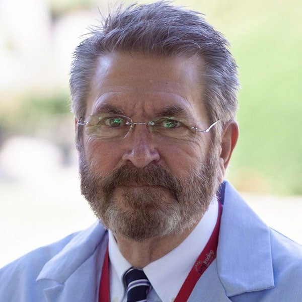 man with short hair, beard and mustache, and glasses, wearing a white shirt, blue neck tie and white lab coat
