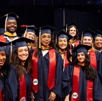 a diverse group of thirteen graduates wearing dark blue caps and gowns and red sashes bearing the UIC logo 