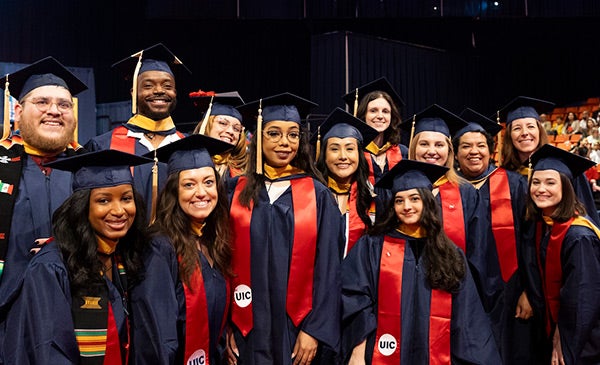 a diverse group of thirteen graduates wearing dark blue caps and gowns and red sashes bearing the UIC logo