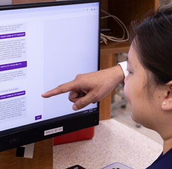 a young woman wearing with long dark hair and wearing dark blue scrubs sitting at a computer and interacting with the chat bot 