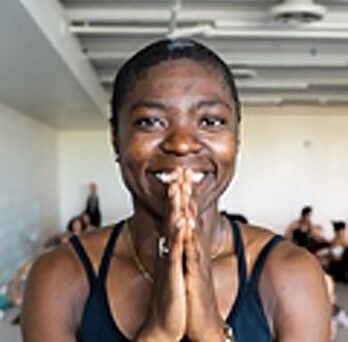 Black woman with very short hair smiling and pressing her palms together near her face 