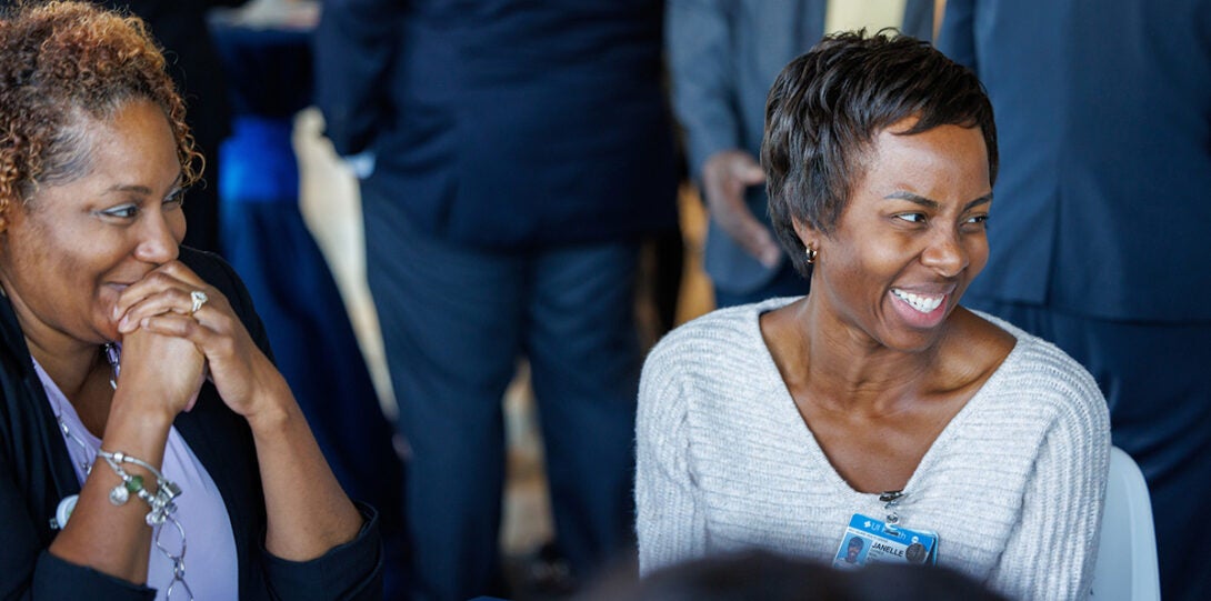 Two African American women sitting at a table and smiling and laughing in conversation