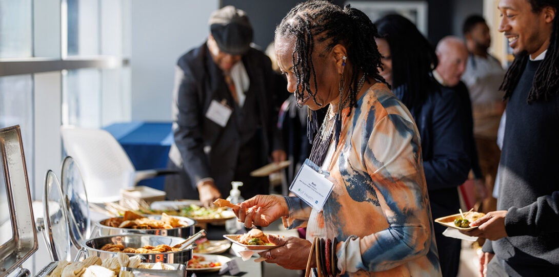 A group of celebration attendees near a buffet. In the foreground is an African American woman looking at the food selection.