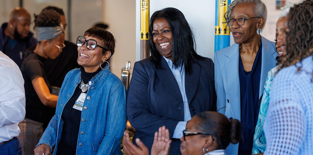 Six African American women smiling, laughing and clapping as they are looking off camera