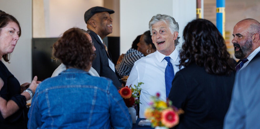 A white man with salt-and-pepper hair smiling as he speaks to a diverse group of women