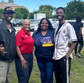 Two African American men and two African American women posing together in an grassy outdoor area on a sunny day 