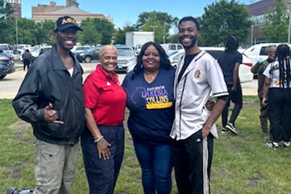 Two African American men and two African American women posing together in an grassy outdoor area on a sunny day