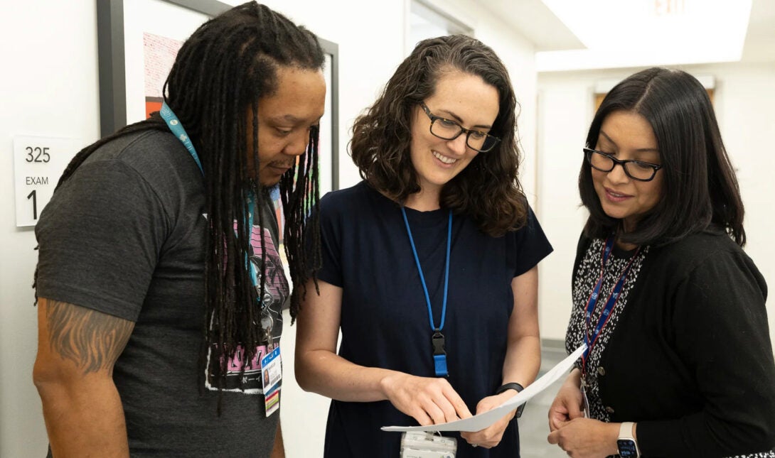 An African American man and two women standing together in a clinical setting as they are reading a report