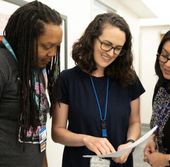 An African American man and two women standing together in a clinical setting as they are reading a report 