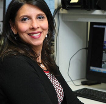 woman in a black suit coat smiling as she sits at a desk with a computer displaying an image of a motor balance study 