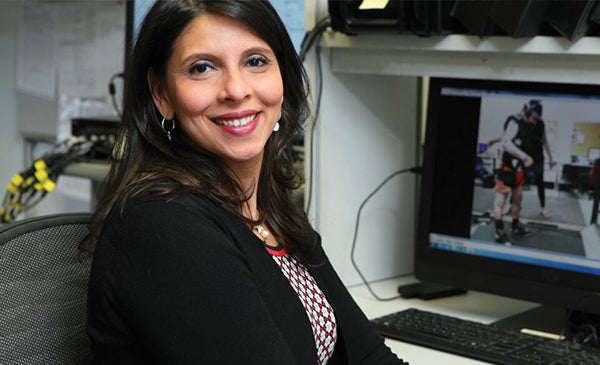 woman in a black suit coat smiling as she sits at a desk with a computer displaying an image of a motor balance study