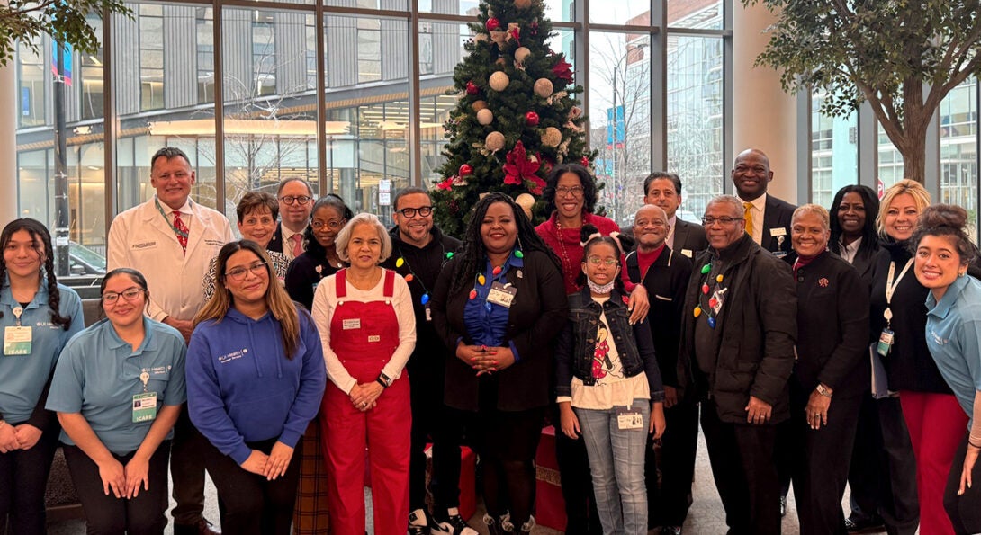 20 people posing together in the hospital atrium in front of a large festive Christmas tree